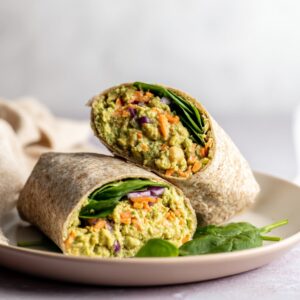 Chickpea avocado salad wrap cut in half showing creamy chickpea filling, carrots, red onion, and spinach inside whole grain tortilla.