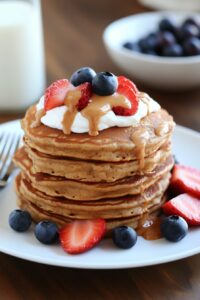 Stack of fluffy Greek yogurt protein pancakes topped with Greek yogurt fresh berries and a drizzle of almond butter on a white plate