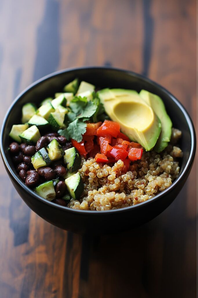 Bowl filled with fluffy quinoa, black beans, sautéed zucchini, roasted red bell peppers, creamy avocado slices, and fresh cilantro—vibrant, high-protein vegan burrito bowl perfect for meal prep.