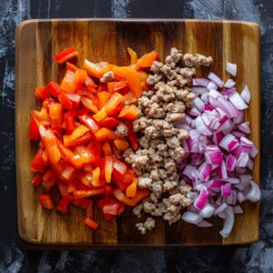 Chopped bell peppers, diced onions, and crumbled turkey sausage laid out on a cutting board—fresh, colorful, and ready to cook for a healthy high-protein breakfast burrito.
