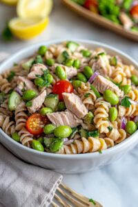 High-protein tuna and edamame pasta salad in a bowl with fresh veggies and lemon dressing, styled for clean eating meal prep.