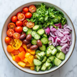 Chopped vegetables being layered into a salad bowl for Mediterranean salad.