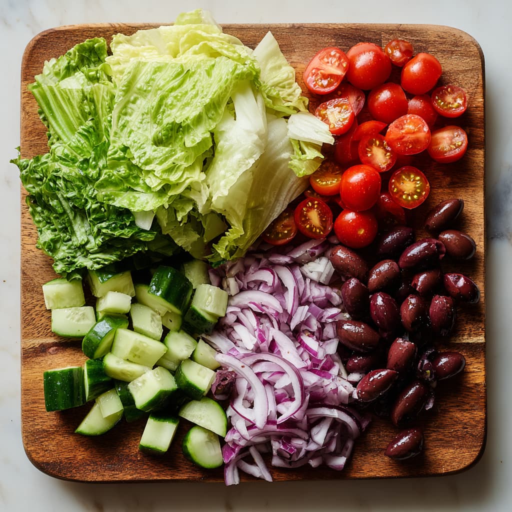 Chopped romaine lettuce, cherry tomatoes, cucumber, red onion, and olives for Mediterranean salad