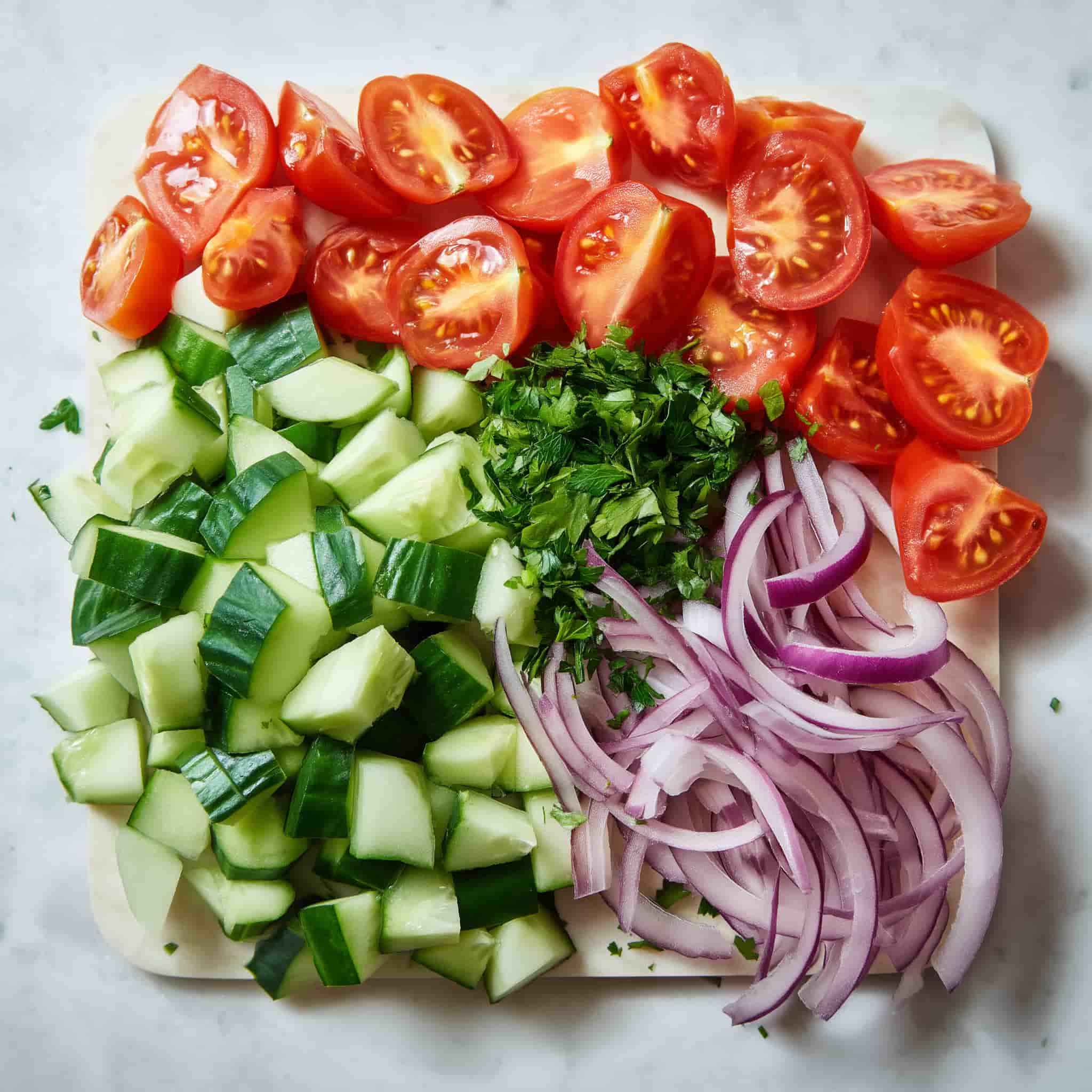 Chopped vegetables including halved cherry tomatoes, diced cucumber, thinly sliced red onion, and fresh parsley prepared for tuna salad