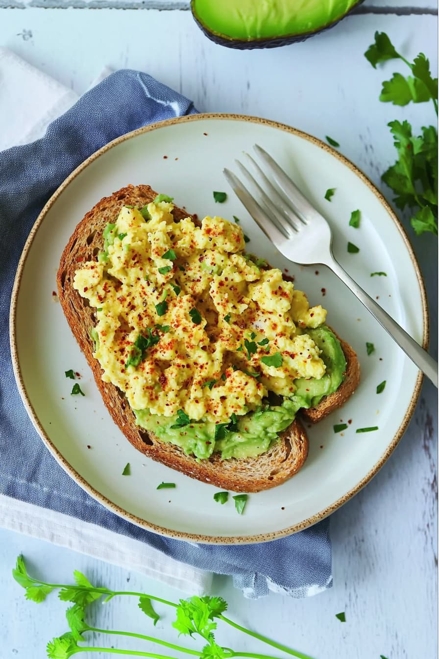High protein scrambled eggs with avocado and whole grain toast on a white plate.