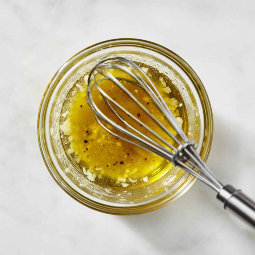 Lemon olive oil dressing with Dijon mustard and minced garlic being mixed in a small bowl, showing smooth and lightly emulsified texture