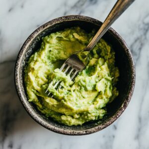 Mashing avocado with lime juice in a bowl for chicken salad base