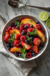 Peach Berry Fruit Salad with sliced peaches, strawberries, blueberries, and raspberries tossed in a fresh honey-lime dressing and garnished with mint.
