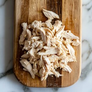 Shredding cooked chicken breast on a cutting board for healthy chicken salad