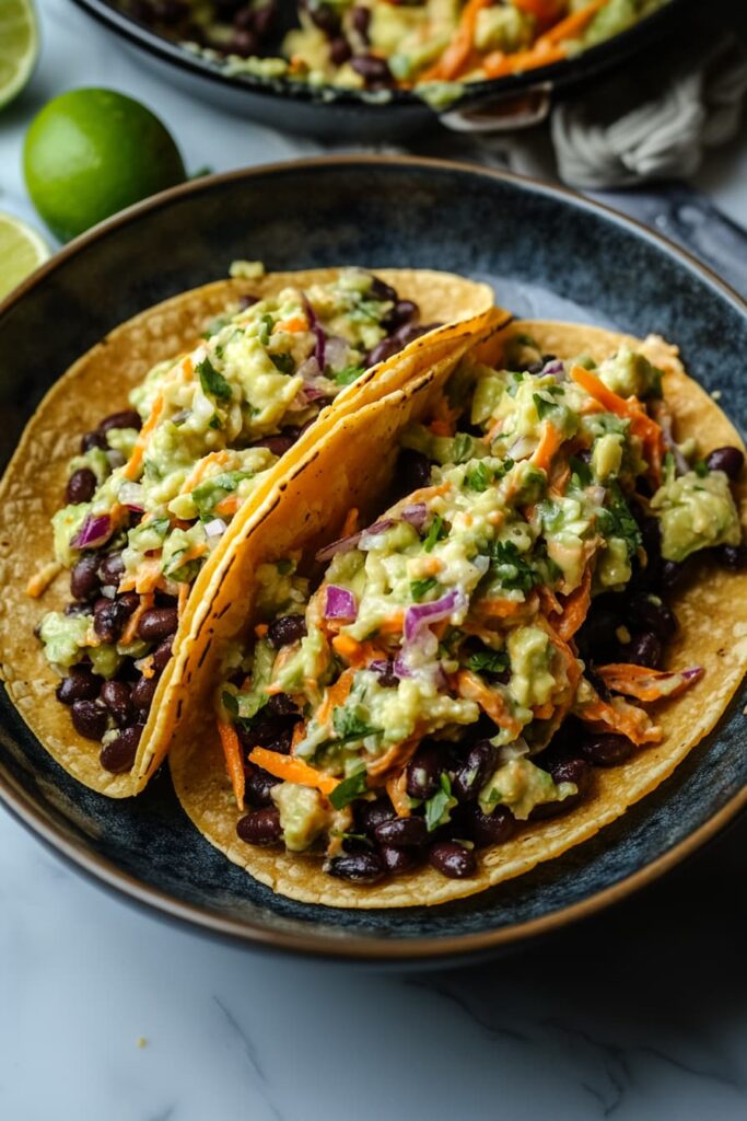 Spicy black bean tacos with avocado slaw, served in corn tortillas and topped with cilantro and lime wedges.