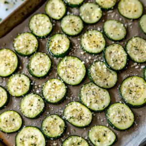 Seasoned zucchini slices laid out on baking sheet for baking