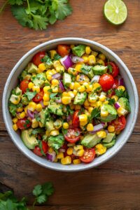 Summer corn salad with avocado, cherry tomatoes, red onion, and cilantro in a bowl, coated with lime and olive oil dressing