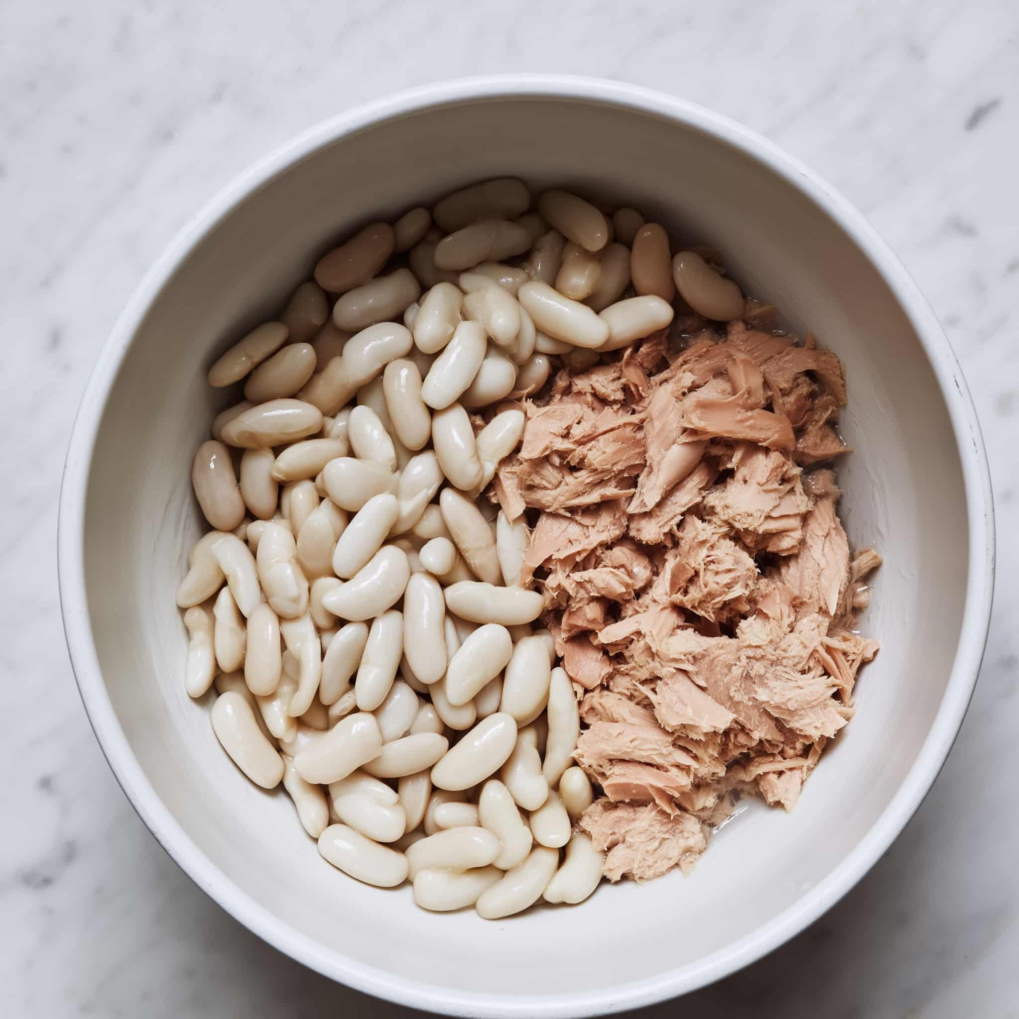 Flaked tuna and rinsed cannellini beans in a mixing bowl, showing soft tuna flakes and plump white beans ready for salad preparation