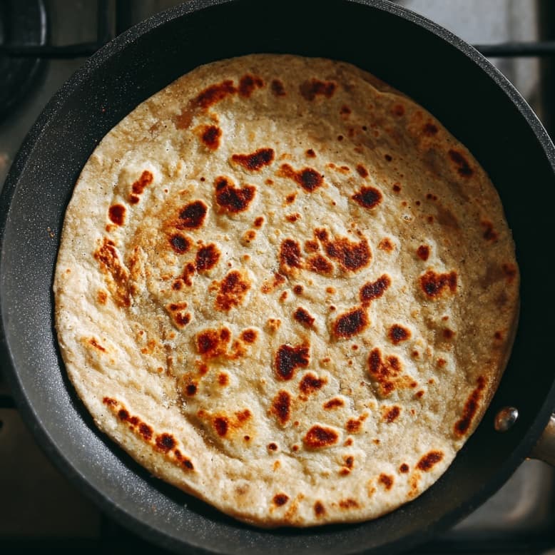 Whole wheat wrap warming in a skillet for assembling the chicken wrap.