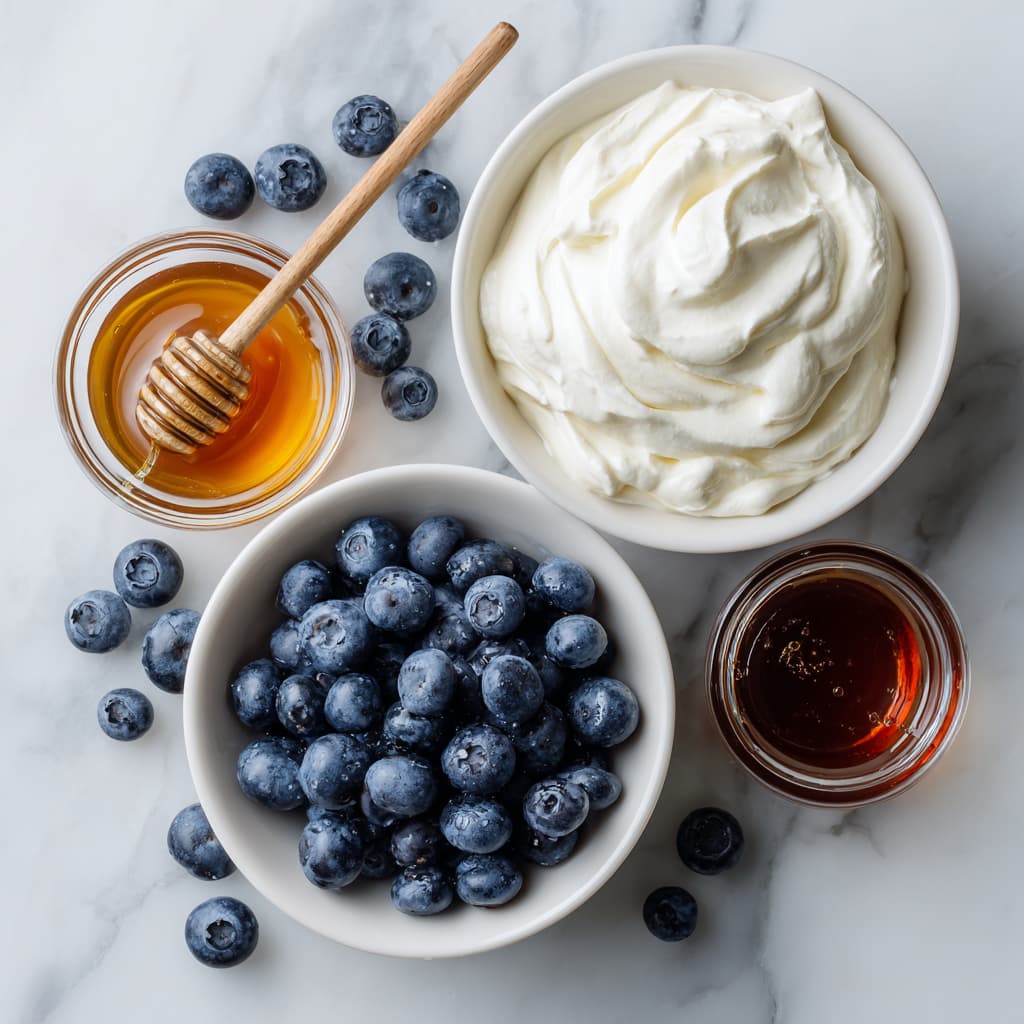 Small bowls of blueberries, honey, Greek yogurt and vanilla extract sitting on a marble surface.