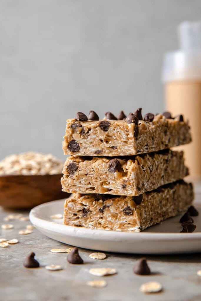Homemade no bake protein bars stacked on plate with oats and chocolate chips.