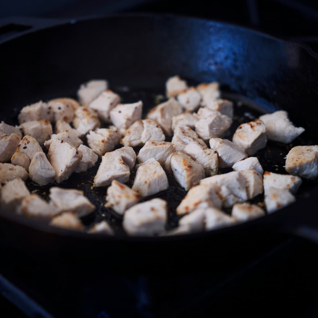Diced chicken breast browning in a skillet with olive oil