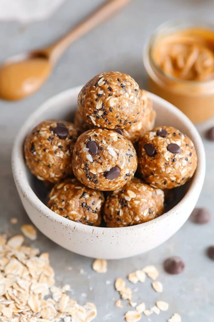 Bowl of no bake oatmeal protein balls made with oats, chia seeds, and chocolate chips on a light surface with scattered oats.