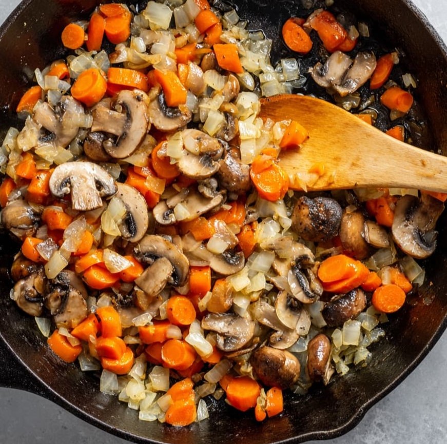 Onions, carrots, and mushrooms cooking together in a skillet