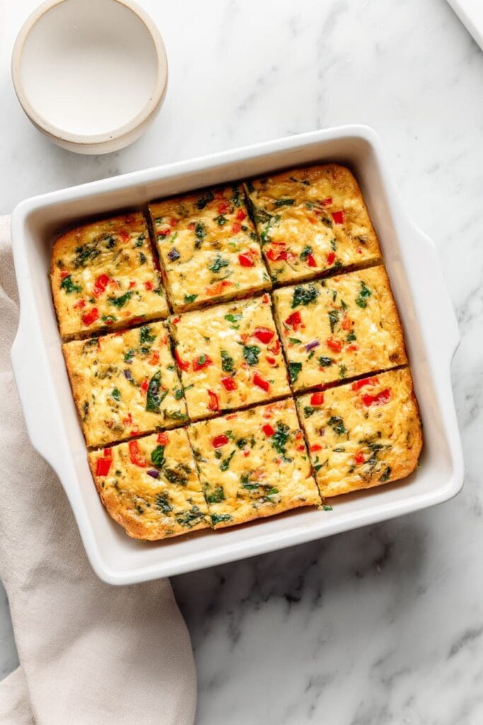 Cottage cheese egg bake sliced into squares with spinach and red bell pepper in a baking dish