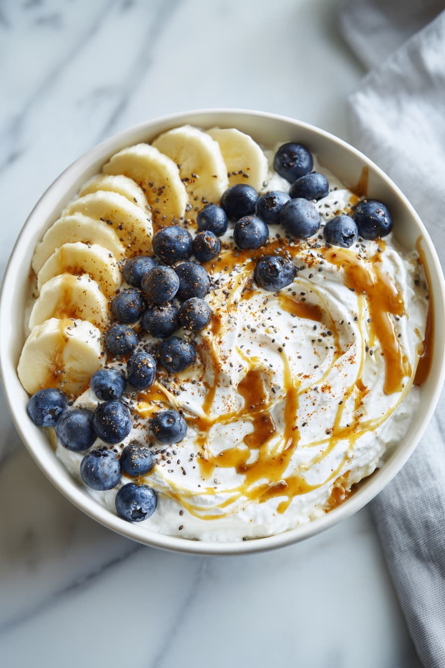 Overhead view of a high protein cottage cheese breakfast bowl topped with banana, blueberries, almond butter, honey, chia seeds, and cinnamon