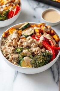Side angle view of a veggie and turkey buddha bowl with quinoa base, roasted vegetables, cooked ground turkey, and tahini sauce, styled for healthy meal prep