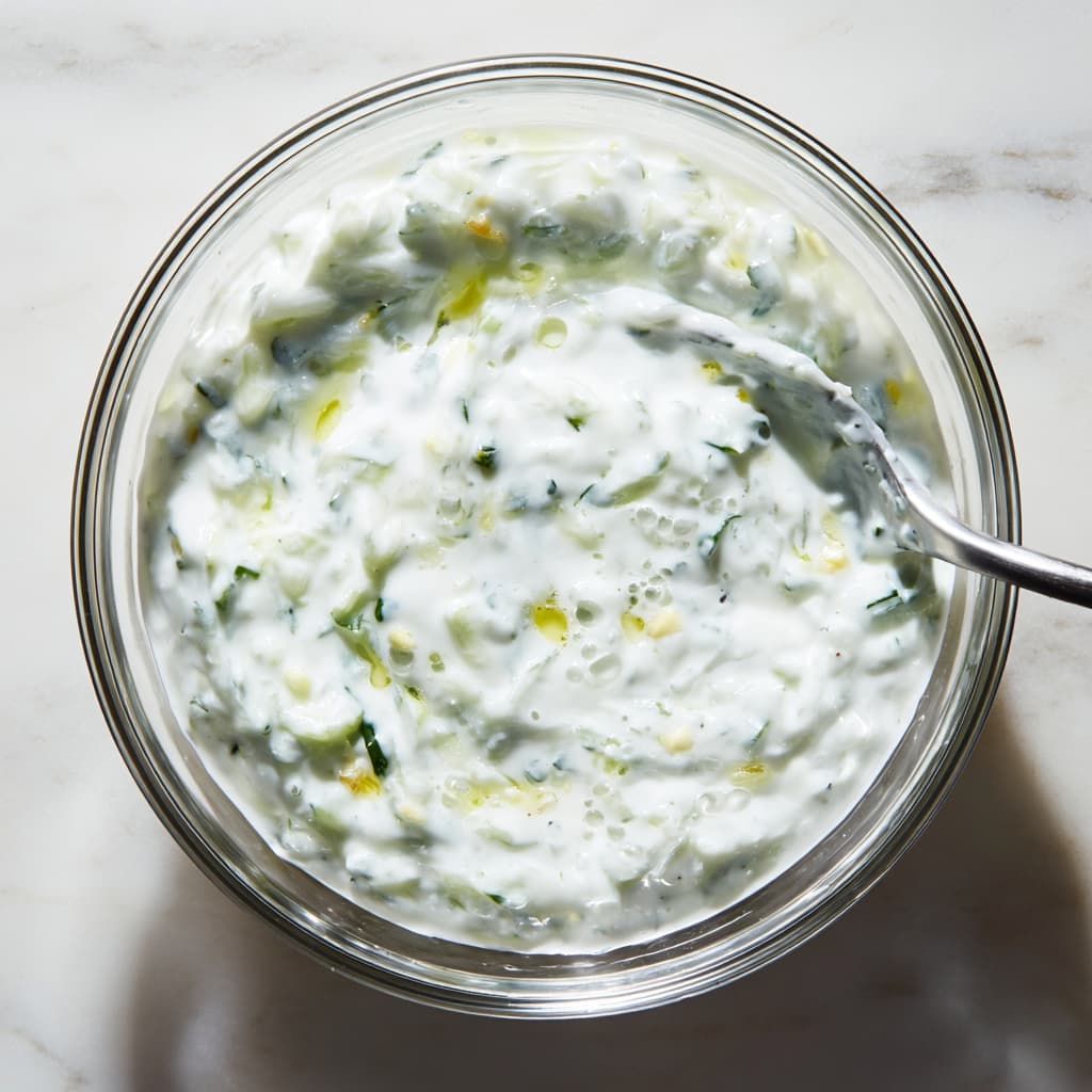 Thick tzatziki sauce made with Greek yogurt, grated cucumber, and garlic in a small glass bowl