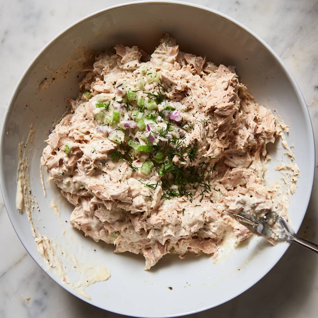 salad mixture topped with chopped celery red onion dill salt and pepper before mixing