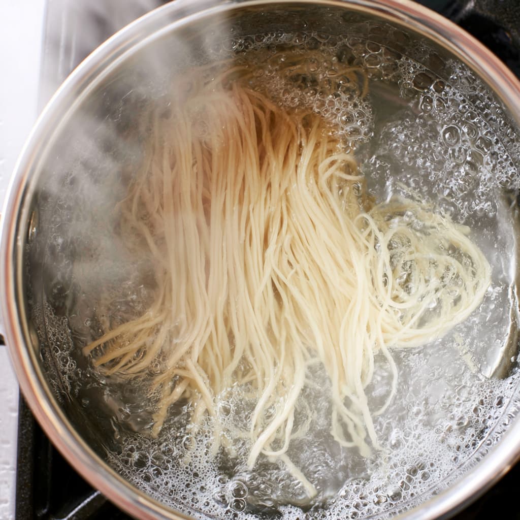 Long strands of pasta cooking in boiling water with light steam rising from the pot