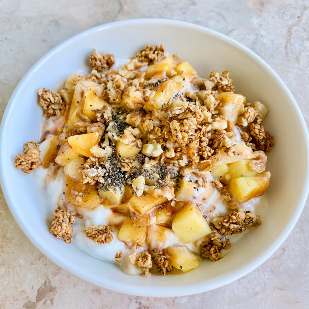 Greek yogurt bowl topped with warm cinnamon apples, granola, walnuts, oats, and chia seeds.