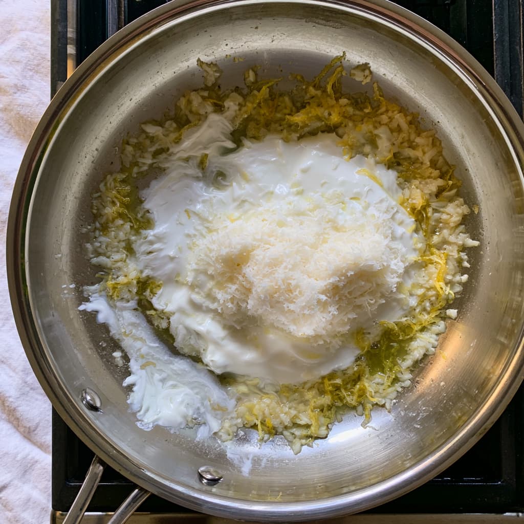 Greek yogurt and grated cheese being stirred into a lemon garlic mixture to create a smooth sauce