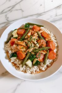 Healthy crockpot chicken with vegetables served over brown rice in a white bowl.