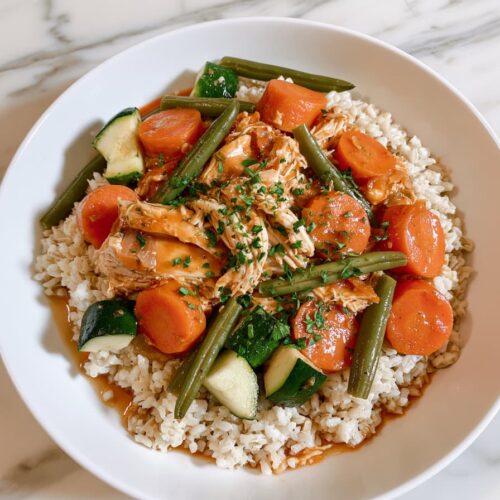 Healthy crockpot chicken with vegetables served over brown rice in a white bowl.