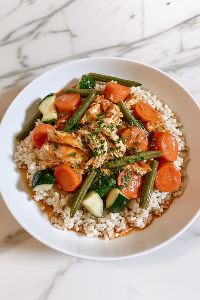 Healthy crockpot chicken with vegetables served over brown rice in a white bowl.
