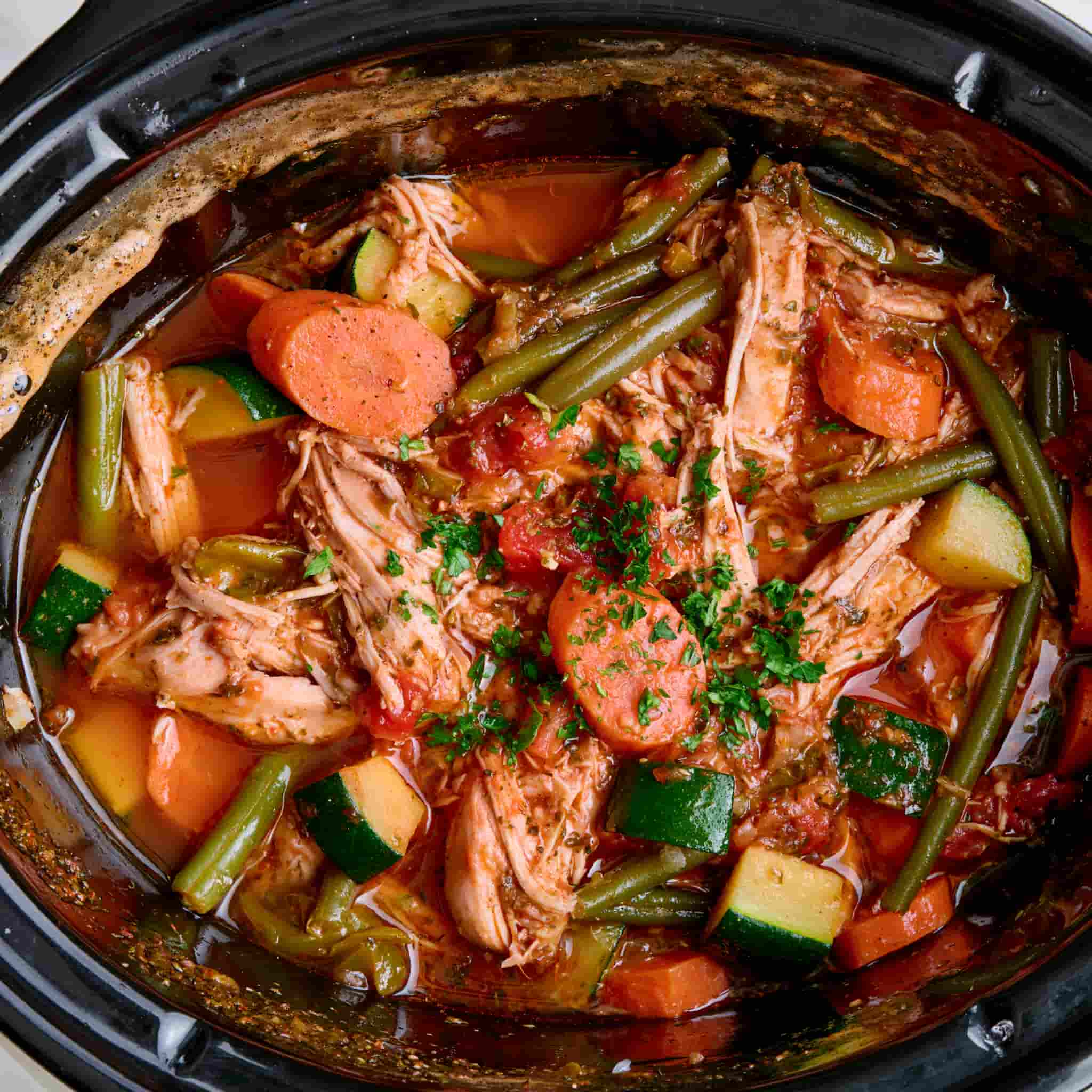 Shredded healthy crockpot chicken mixed with vegetables and garlic herb broth.