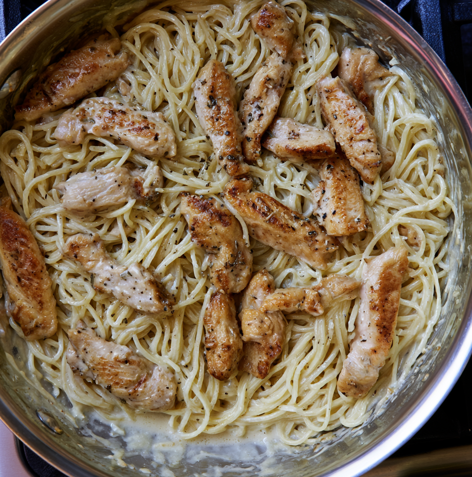 Cooked pasta and sliced chicken mixed together in a creamy sauce inside a pan