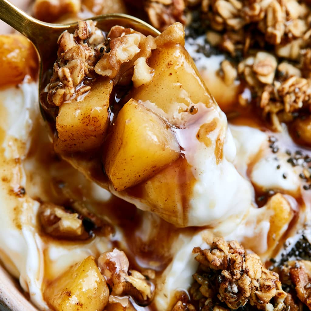 Greek yogurt bowl topped with warm cinnamon apples, granola, walnuts, oats, and chia seeds.